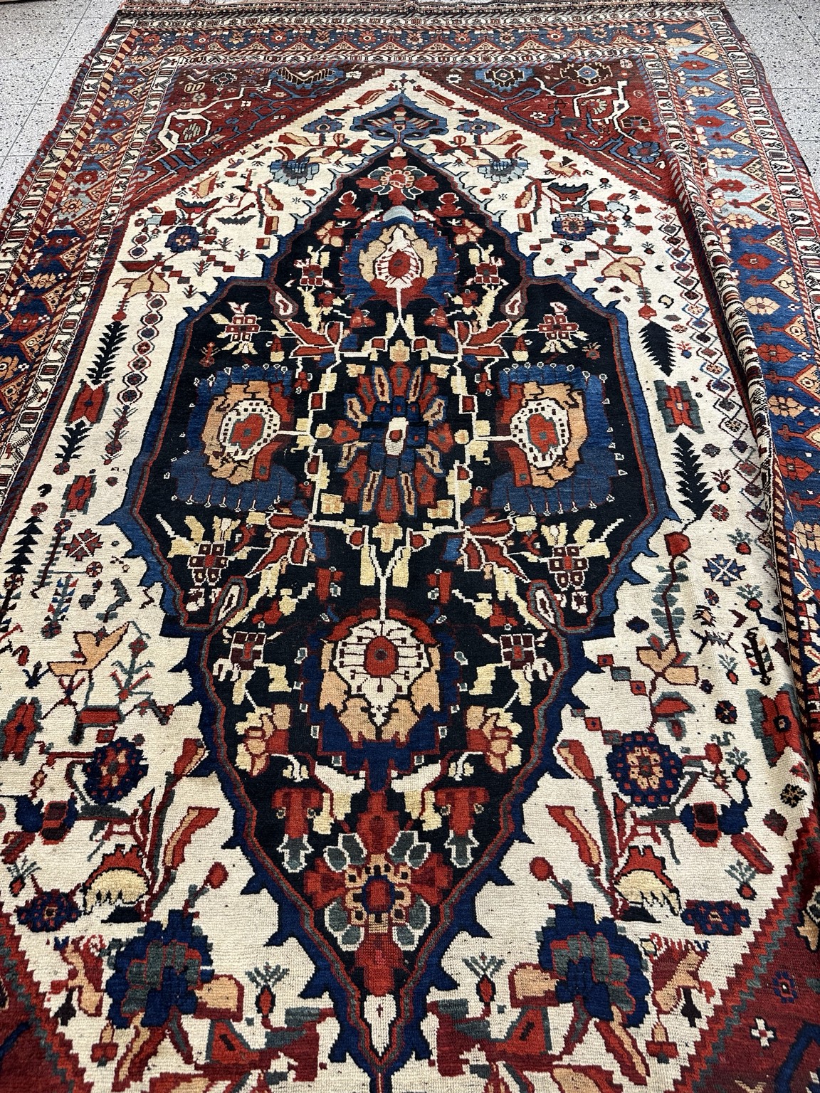 Antique Ghashghai wool rug with geometric designs, a dark blue central medallion, ivory field and red border