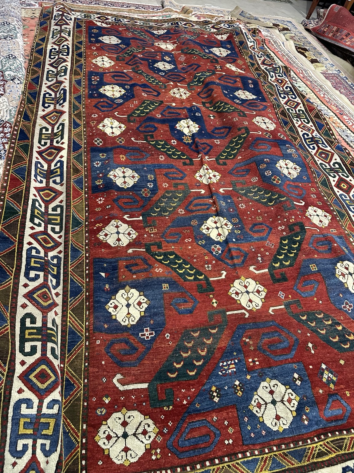 Antique 19th-century Caucasian Pinwheel rug with blue and green geometric motifs, ivory rosettes and an ivory border on a red field